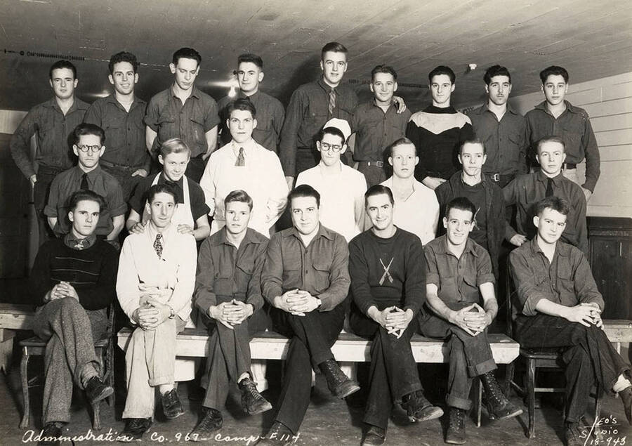 Group portrait of CCC men from Cataldo CCC Camp taken in the barracks. Writing on the photo reads: 'Administration Company 967 Camp F-114. Leo's Studio'.