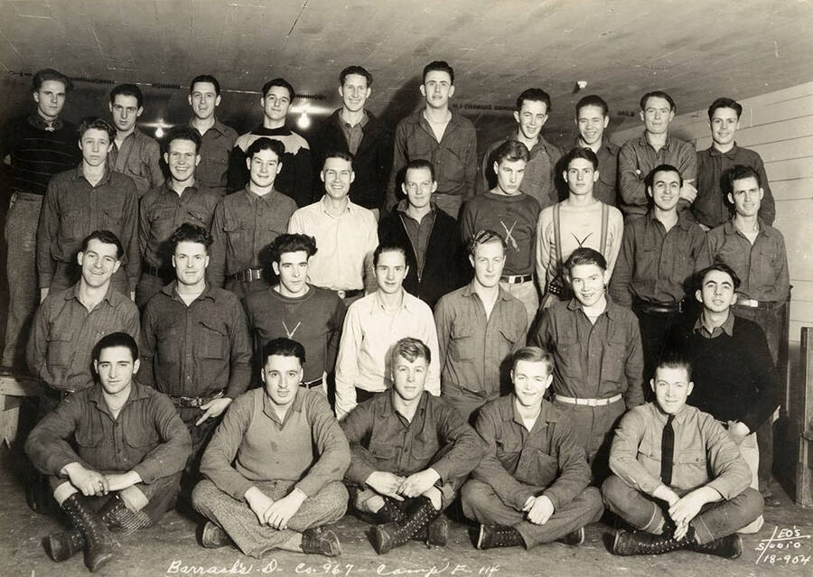 Group portrait of CCC men from Barracks D in the Cataldo CCC Camp. Writing on the photo reads: 'Barracks D Company 967 Camp F-114 Leo's Studio'.