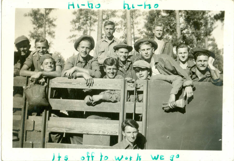 Photo form album shows group shot of crew in trucks. Handwritten caption 'Hi-ho hi-ho Its off to work we go'.  This is likely to be located at Camp Creek, South Fork of the Salmon River, which built Krassel Ranger Station.