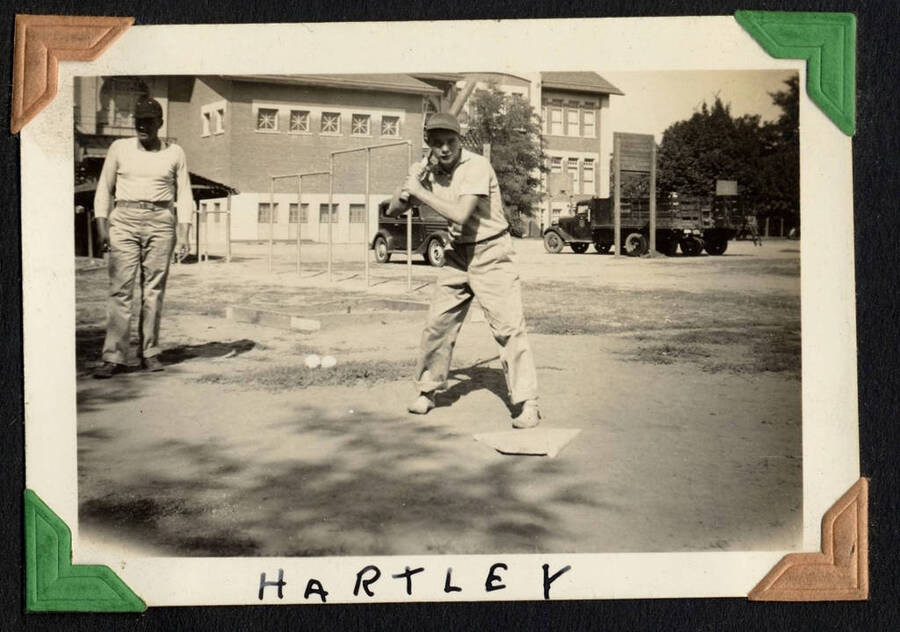 Picture of man standing with a bat, with large building in background. From the Paul Saft photographic album, SCS-1, C-1503, 1938-19, depicting camp life, taken mostly in the Moscow, Lewiston, Robinson Lake area, 1938-19
