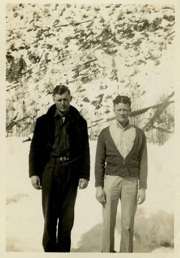 Two men stand in the snow, facing the camera. Back of photograph reads, "Bill Logan + Mayland Camp N.F."
