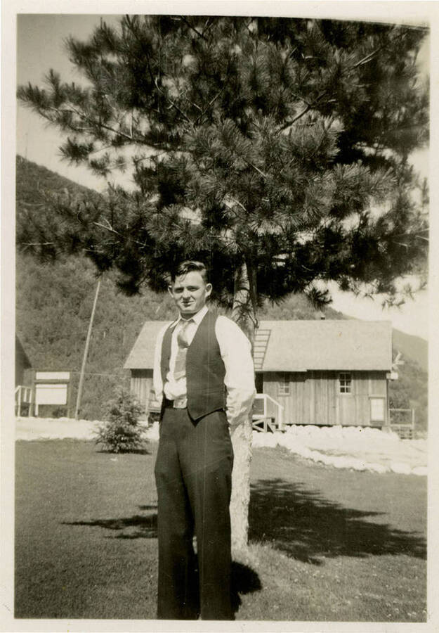 Possibly William Ross posing for a photograph in front of a large tree. He wears a dress clothes. Back of photograph reads, "William Ross CCC co.5702."