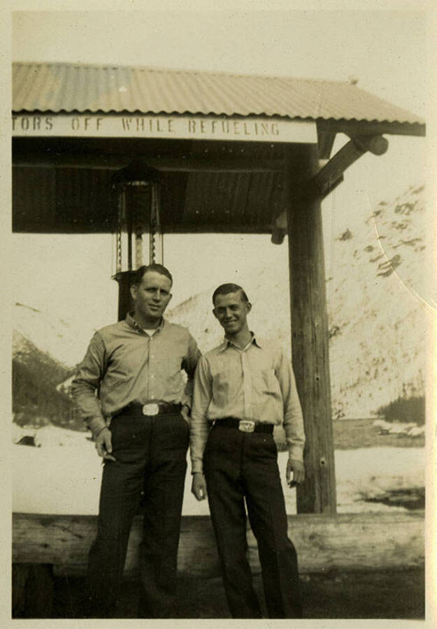 Two men, Herric and Morris, stand near an outdoor awning. Back of photograph reads, "Herric and Morris."