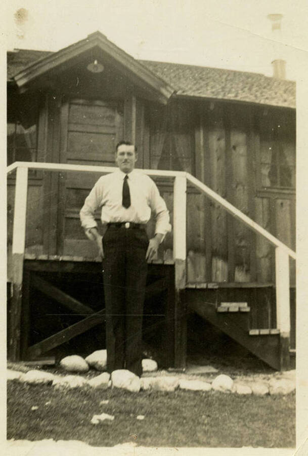Possibly Louis Brown standing in front of a wooden building. He is wearing a tie. Back of photograph reads, "Louis Brown North Fork"