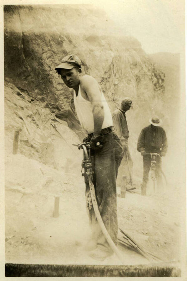 A photograph a man, possibly Ross, holding a jack hammer. Two other figures can be seen in the background also holding tools. Back of photograph reads, "Ross CCC Co. 5702."