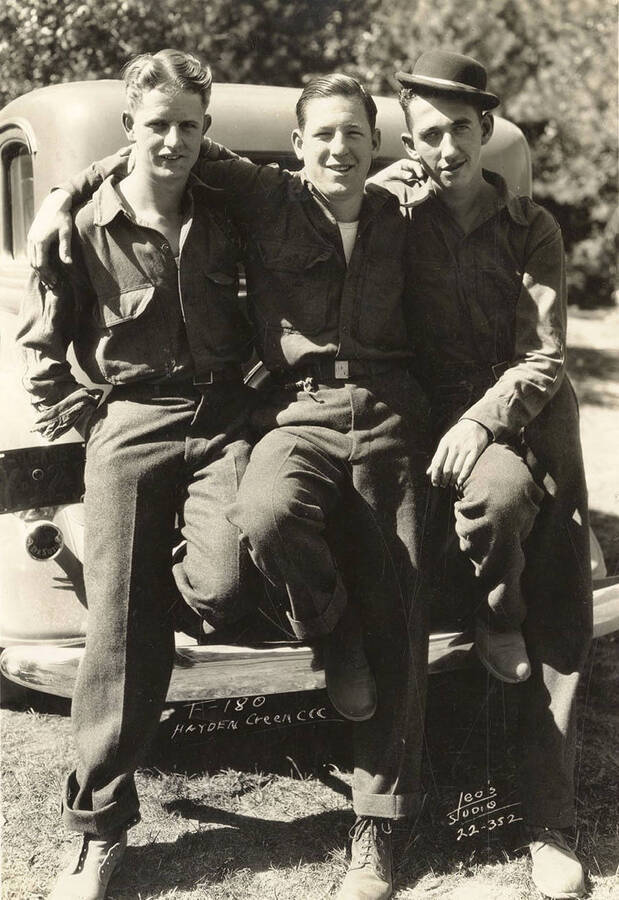 Group portrait of three CCC men seated on an automobile at Hayden Creek CCC Camp. Writing on the photo reads F-180 Hayden Creek CCC Leo's Studio'.