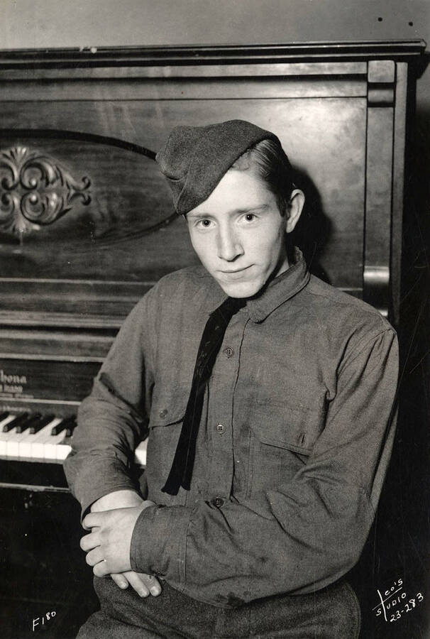 Portrait of a CCC man in front of a piano at Hayden Creek CCC Camp. Writing on the photo reads: 'F-180 Leo's Studio'.