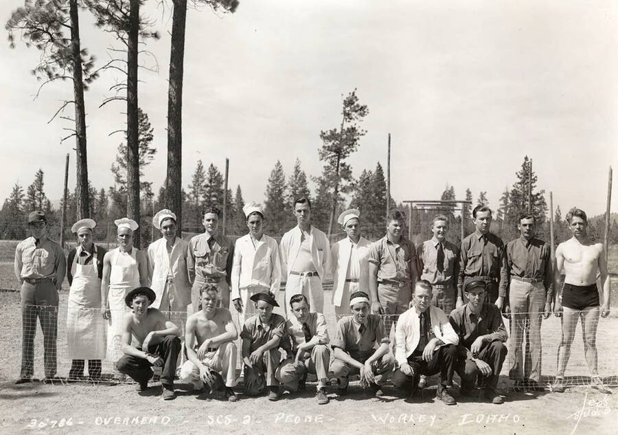 Group portrait of CCC men, K. P.'s, cooks, and other individuals at the Peone CCC Camp in Worley, Idaho, note the man in the bathing suit. Writing on the photo reads: 'Overhead SCS-2 Peone Worley, Idaho Leo's Studio'.