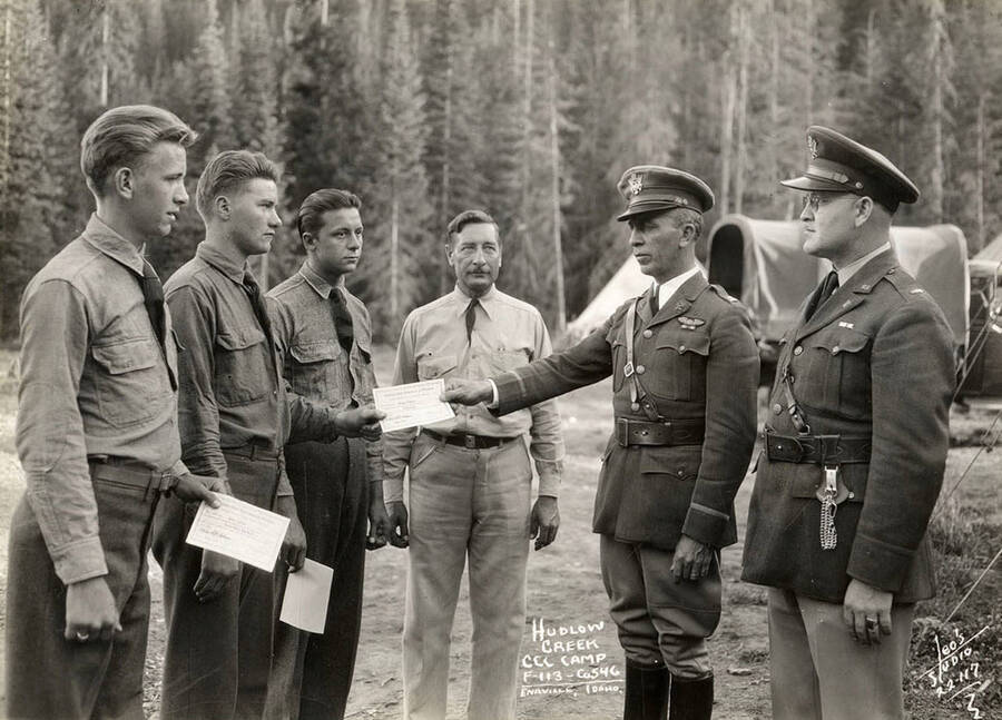 Photo of officers handing certificates to three CCC men at Hudlow Creek CCC Camp, F-113, Company 546. Writing on the photo reads: 'Hudlow Creek CCC Camp F-113 Company 546 Enaville, Idaho Leo's Studio'.