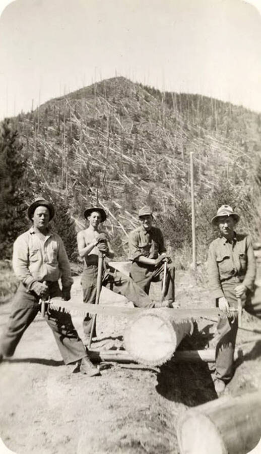 Four CCC men pose with a log and crosscut saw. Back of photo reads: '1935 Scars of 1910 Fire Ingerlund, Smith, Homer Jacobs, Pappy Dejarnette between Magee R.S. and Independence Cr.