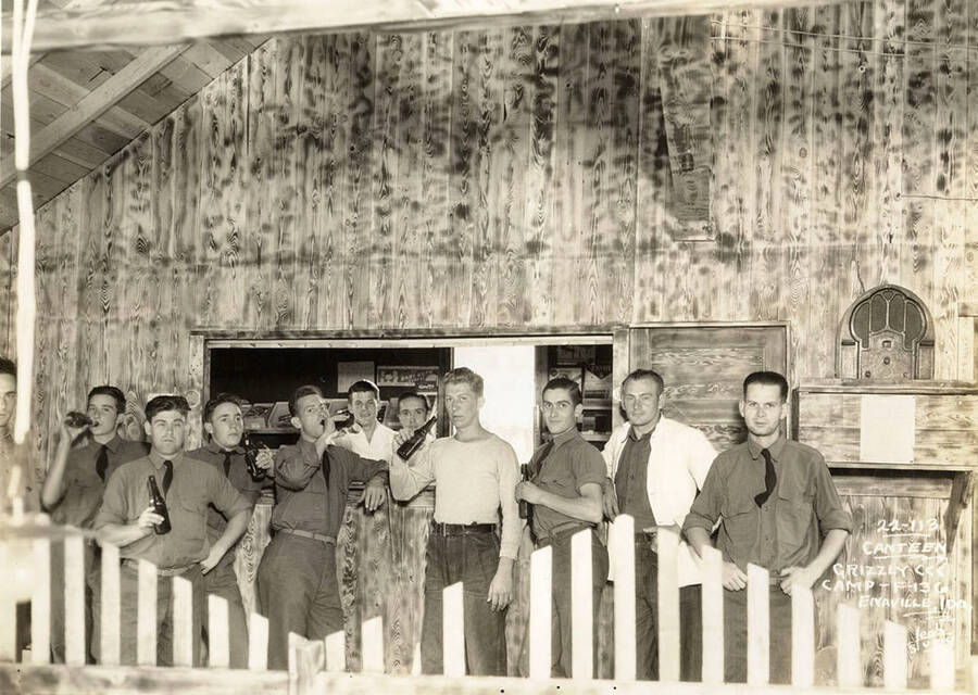 Group portrait of CCC men drinking at the Canteen in Grizzly CCC Camp F-136. Writing on the photo reads: 'Canteen Grizzly CCC Camp F-136 Enaville, Idaho. Leo's Studio'.