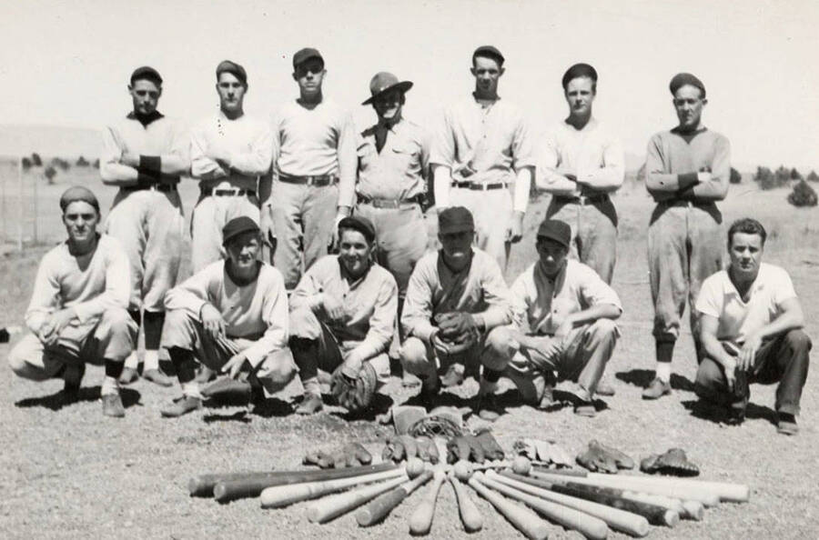 Magee CCC Camp Company 544 baseball team posed for a team photo with gloves, balls, and bats in the foreground. Back of photo reads: 'Coeur d'Alene National Forest CCC Company 544 Baseball Team 1935-1937' some of the players shown are listed as 'R. Hardin (KY), Rex Quesenberry, Verne, Felker, and McKeown'.