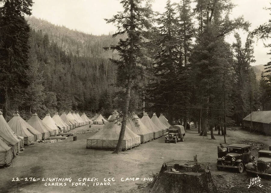 View of Lightning Creek CCC Camp, F-111. Note transport truck and two automobiles. Writing on the photo reads: 'Lightning Creek CCC Camp F-111 Clarks Fork, Idaho. Leo's Studio'.