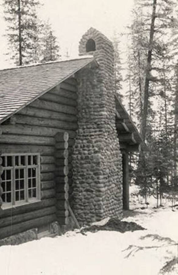 View of a rock chimney at the end of a cabin at CCC Camp Kalispell Bay, F-142. Back of photo reads: 'Kalispell Bay F-142'