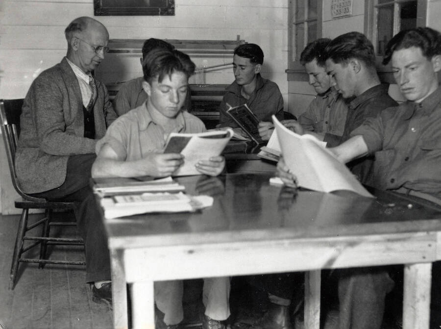Several CCC men sit around a table reading while attending a class at Camp Heyburn.
