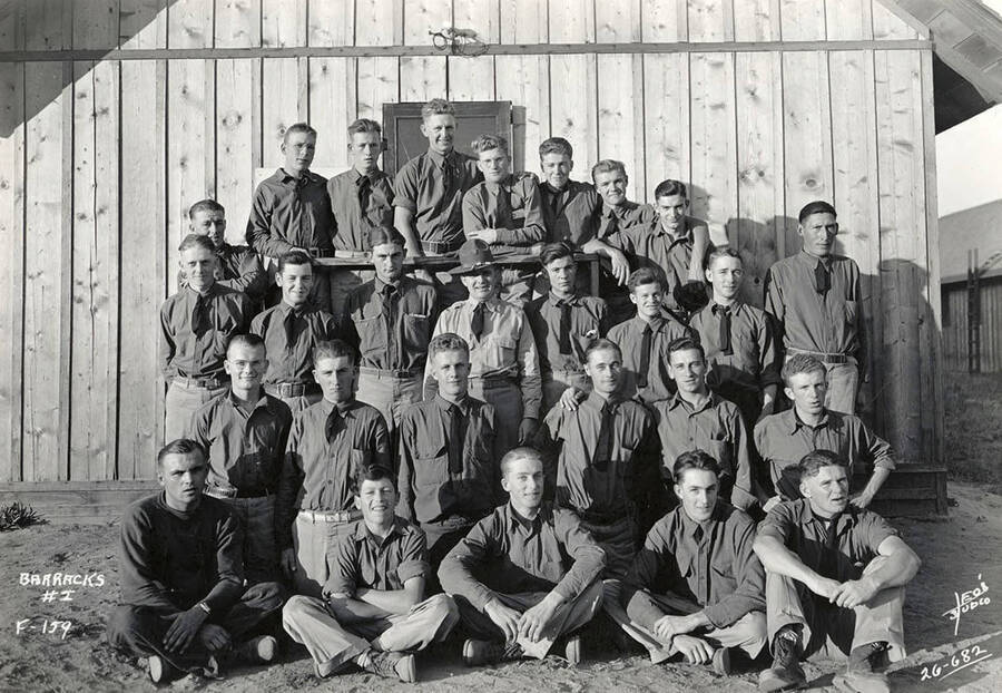 Group photo of the CCC men staying in Barracks 1 at the Blow Down 2 CCC Camp. F-159. Writing on the photo reads: 'Barracks #I F-159 Leo's Studio'.