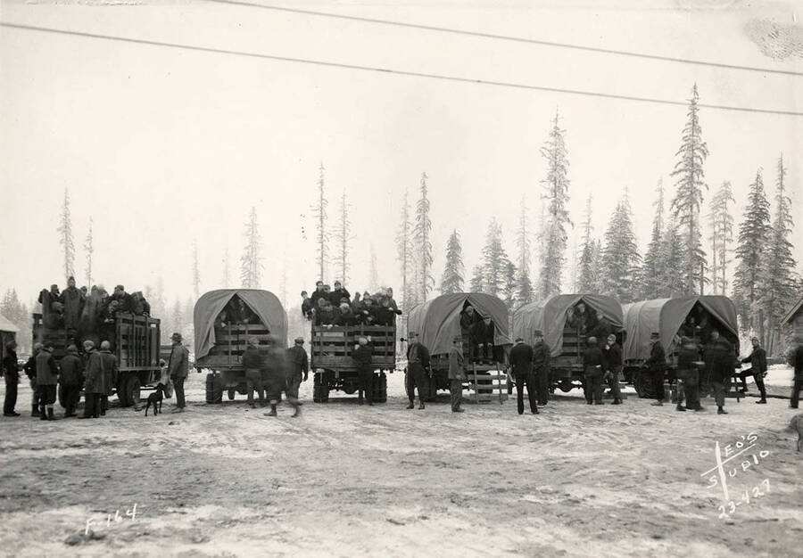 Six trucks loaded with CCC men at the Four Corners CCC Camp, F-164. Writing on the photo reads: 'F-164 Leo's Studio'. Back of photo reads: 'Four Corners Priest River Kaniksu, National Forest'.