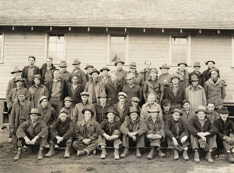Group photo outside one of the Kalispell Bay CCC Camp, F-142, barracks. Writing on the photo reads: 'Leo's Studio'. Back of photo: 'Kalispell Bay'.