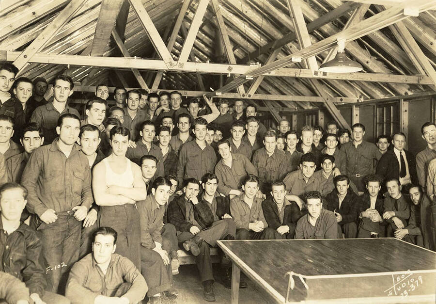 Group photo of CCC men inside the Recreation Hall at CCC Camp Kalispell Creek, F-102. Writing on the photo reads: 'F-102 Leo's Studio'. Back of photo reads: 'Kaniksu'.