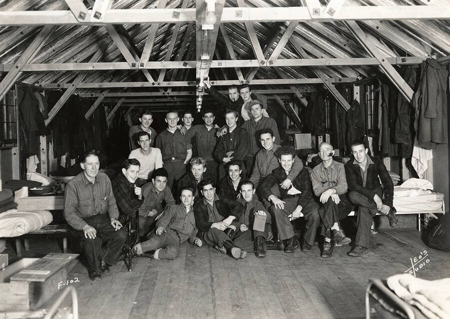 Group photo of CCC men inside a barrack at Kalispell Creek CCC Camp, F-102. Writing on the photo reads: 'F-102 Leo's Studio'. Back of photo reads: 'Kaniksu'.