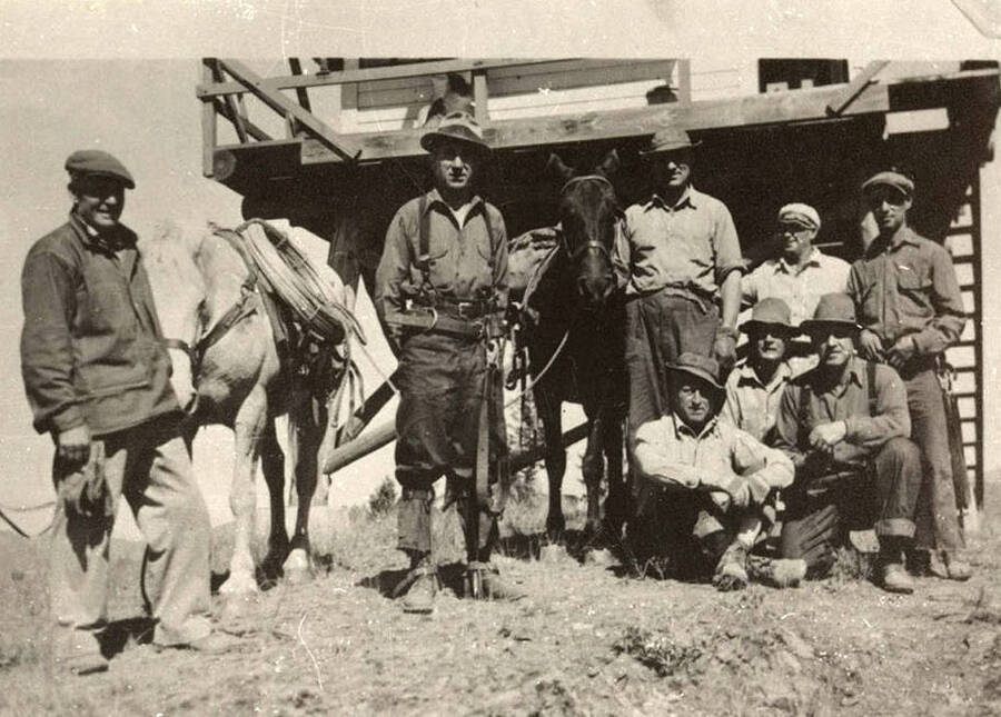 Group photo of a CCC Construction crew and their workhorses in front of the Fire Lookout Tower on [Proten] Mountain. Back of the photo reads: 'CCC tower construction and telephone construction crews on [Proten] Mountain. About 1935. Leo Black Photo. Chuck Peterson copy.'