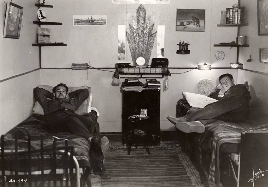 Two CCC men lounging in their dorm room at Four Corners CCC Camp, F-164.  Writing on the photo reads: 'Leo's Studio'. Back of photo reads: 'Four Corners Priest River Kaniksu, National Forest'.