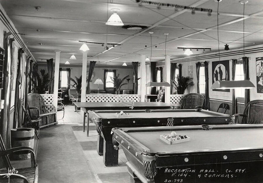 Interior view of the Recreation Hall with two pool tables and a ping pong tables at Four Corners CCC Camp, F-164. Writing on the photo reads: 'Leo's Studio Recreation Hall Company 594 F-164 4 Corners'. Back of photo reads: 'Four Corners Priest River Kaniksu National Forest'.