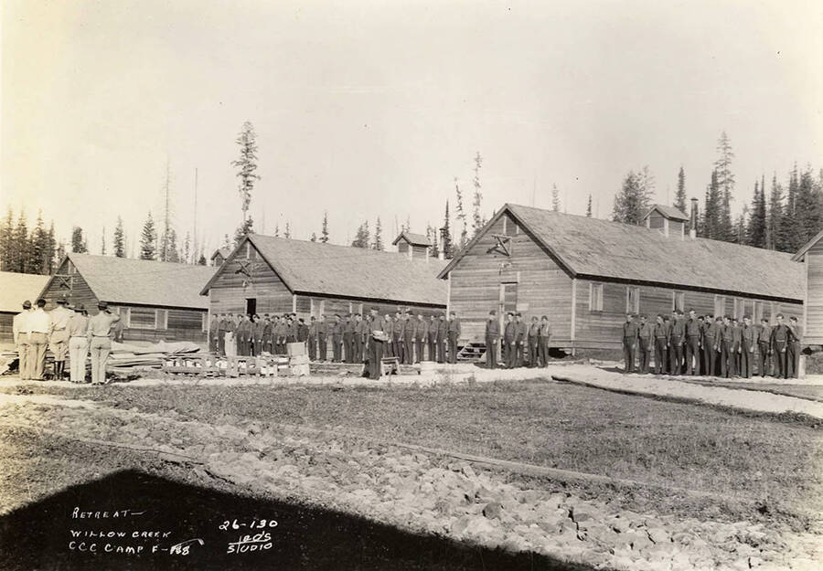 Group photo of CCC men at attention for retreat of the flag at Willow Creek CCC Camp. Writing on the photo reads: 'Retreat Willow Creek CCC Camp F-188 Leo's Studio'.