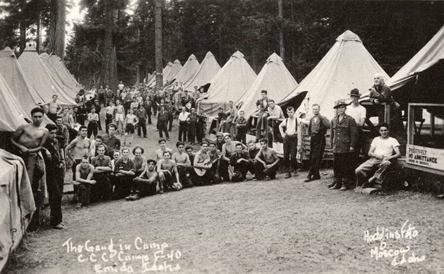 Group photo of CCC men in the CCC Camp Santa Creek, F-40, near Emida, Idaho. The sign on the tent reads: 'Positively No Admittance except on business'. Writing on the photo reads: 'The gang in camp CCC Camp F-40 Emida, Idaho Hodgins Foto Moscow, Idaho'.