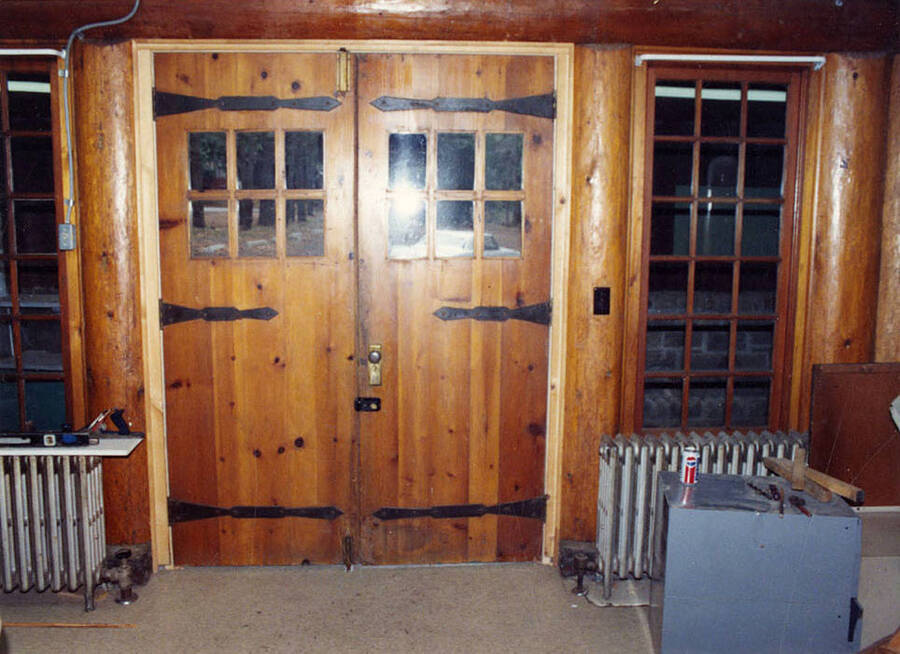 Interior view of Lodge doors with radiators, tools, and a Pepsi can. An automobile can be seen through the windows on the door. The doors were built by the CCC Back of photo reads: 'Rocky Point Lodge Doors Ken Hart'. Ken Hart was a member of Company 1995
