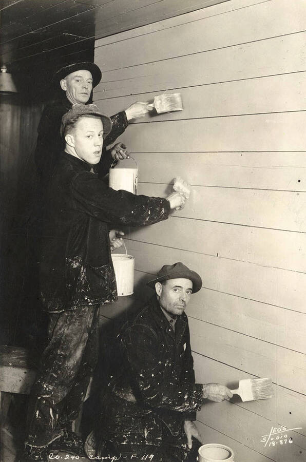 Three CCC men posed while painting a wall on the inside of a building at Marble Creek CCC Camp. Writing on the photo reads: ' Company 240 Camp F-117 Leo's Studio'. Back of photo reads 'Marble Creek'.