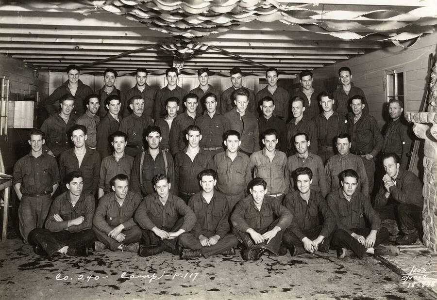 Group photo of CCC men posed in a building at Marble Creek CCC Camp, F-117. Writing on the photo reads: ' Company 240 Camp F-111 Leo's Studio'. Back of photo reads 'Marble Creek'.