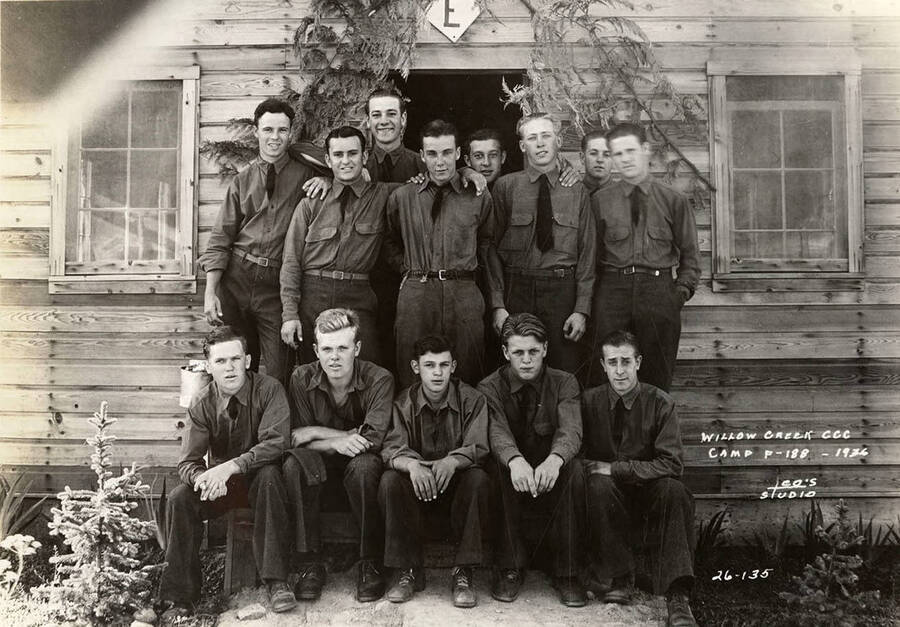 Group photo of CCC men posed outside of barrack 'E' at Willow Creek CCC Camp, F-188. Writing on the photo reads: 'Willow Creek CCC Camp F-188 1936 Leo's Studio'.