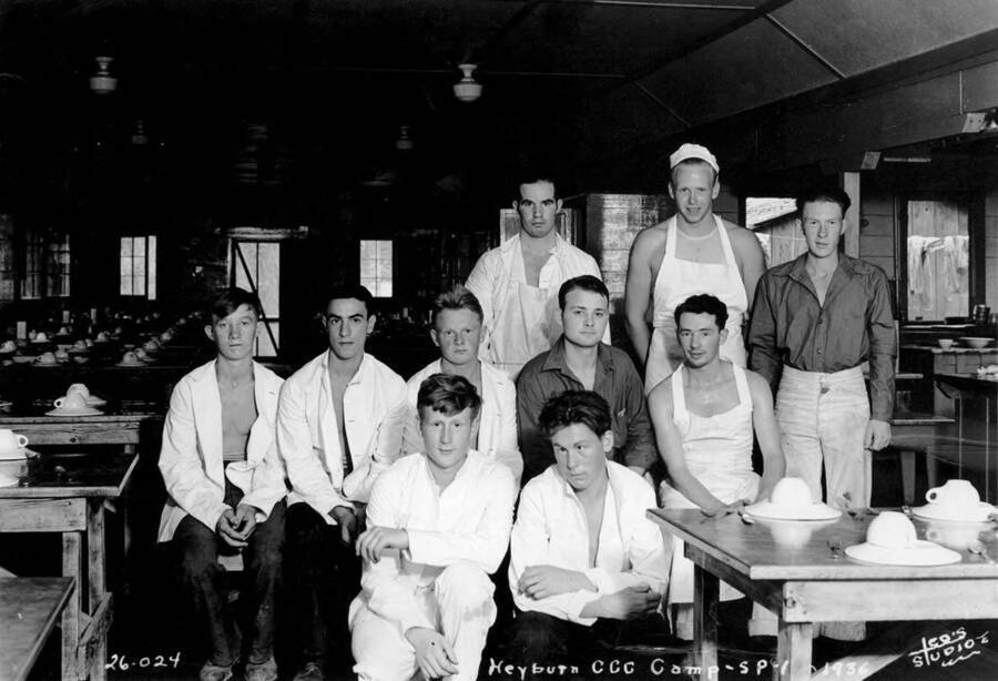 Group photo of CCC Camp Heyburn cooks and K.P.s posing in the dining hall, SP-1, Company 1995. From left to right: Front Row: Two unidentified men. Middle Row: unidentified man, Paul Lahaih, Milsen Kellner from Dover, Idaho, Gerald D. Stewart, Harry J. Nelson. Back row: Joe Deroshia from Sagle, Idaho, Morton Rolf from Bonners Ferry, Idaho, and Fred H. Blood from Sandpoint, Idaho. Writing on the photo reads: Heyburn CCC Camp SP-1 1936 Leo's Studio.