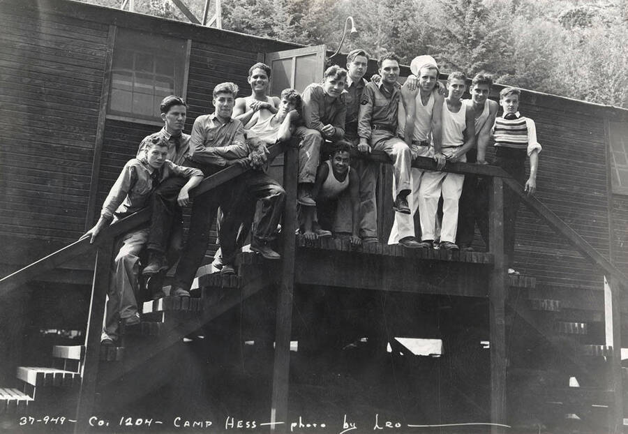 Group of CCC men posing for a photo on a stair railing outside of a building at CCC Camp Hess, F-204, Company 1204. Writing on the photo reads: 'Company 1204 Camp Hess photo by Leo'. Back of photo reads 'Camp Hess St. Joe'.