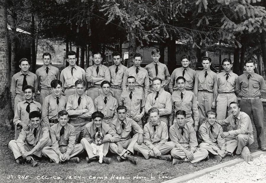 Group of uniformed CCC men posed for a photo with a dog at CCC Camp F-204, Company 1204. Writing on the photo reads: 'CCC Company 1204 Camp Hess photo by Leo'. Back of photo reads: 'Camp Hess St. Joe'.