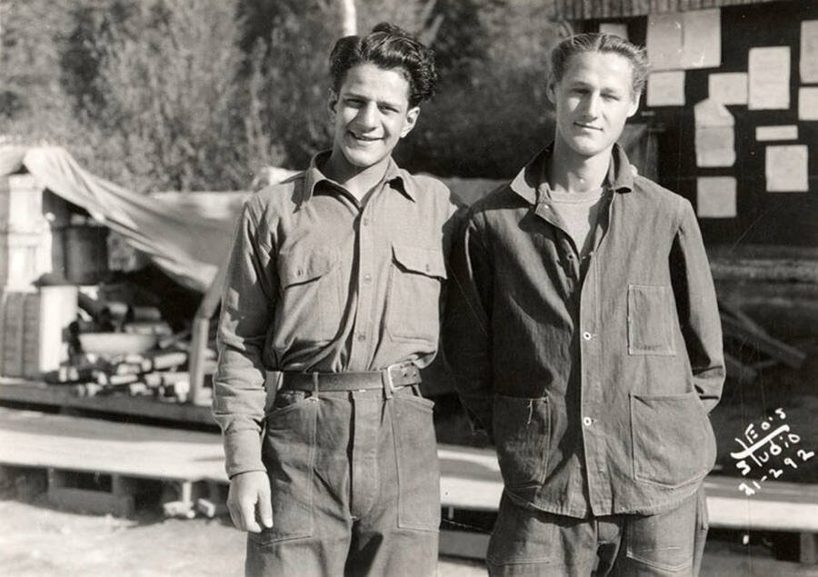 Two CCC men posed for a photo at Merry Creek CCC Camp, F-140, in front of a bulletin board and supplies. Back of photo reads: 'St. Joe'.