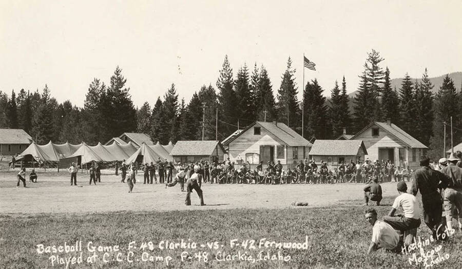 Photo of a CCC baseball game between Clarkia CCC Camp, F-48, Company 1276 (home), and Fernwood CCC Camp, F-42, Company 1202 (visitors). Writing on the photo reads: 'Baseball Game F-48 Clarkia vs. F-42 Fernwood played at CCC Camp F-48 Clarkia, Idaho. Hodgins Foto Moscow, Idaho'. Back of photo reads: 'Clarkia, Idaho 1933'.