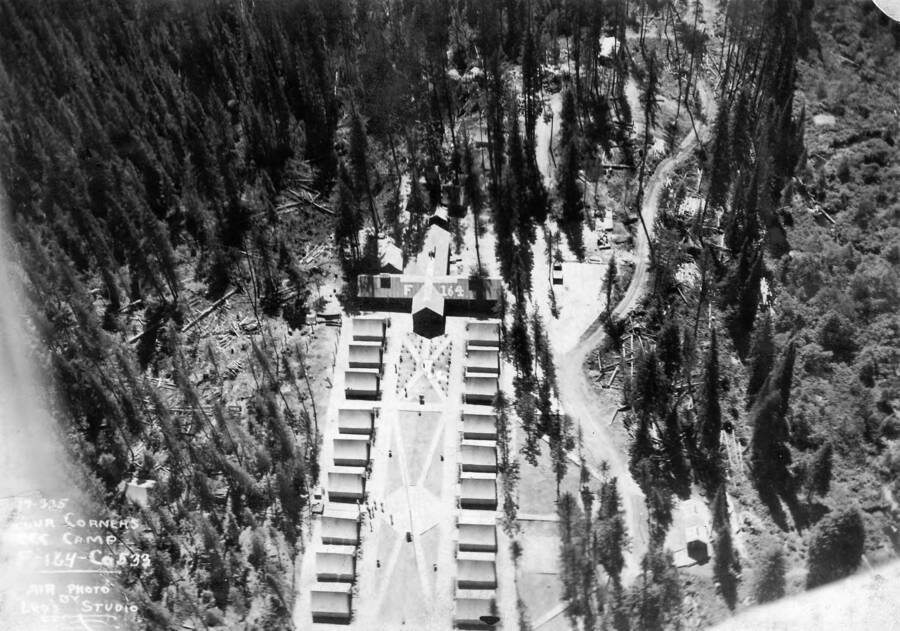 An aerial view of Camp Four Corners, F-164, Company 533, Priest River, Idaho. Writing on the photo says: 'Four Corners CCC Camp F-164 Co. 533 Air photo by Leo's Studio.' Roof of main building reads 'F-164'.