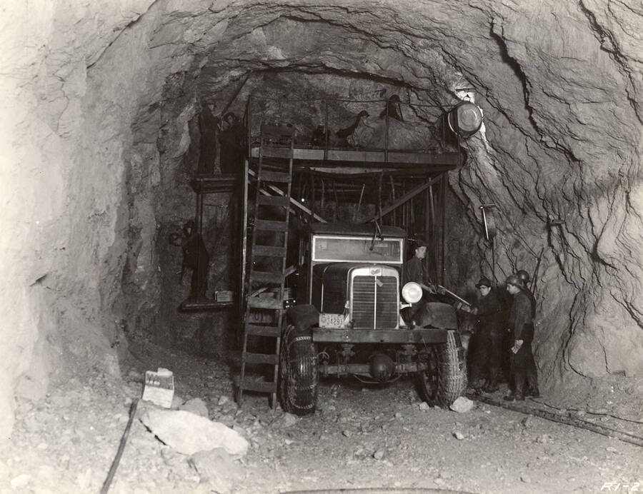 Scaffolding surrounds a truck as CCC men work on the Fishhook Tunnel. Note that the tires of the truck have been outfitted with chains and the box of dynamite on the left of the photo. Back of photo reads: 'Fishhook Tunnel 1938 E-Roads (e)-36 CCC'. Stamp on back of photo reads: 'If this photo is reproduced credit must be given as follows: 'Photo by K.D. Swan, courtesy U.S. Department of Agriculture, Forest Service.''