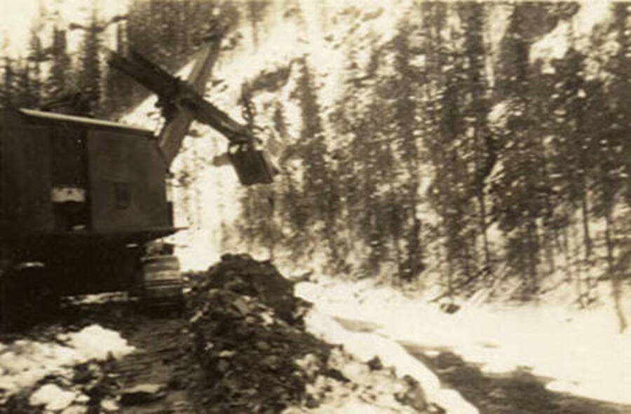 A power shovel works along a creek in the snow. Back of the photo reads: 'Bay City Diesel engine shovel. Idaho March 1939.'