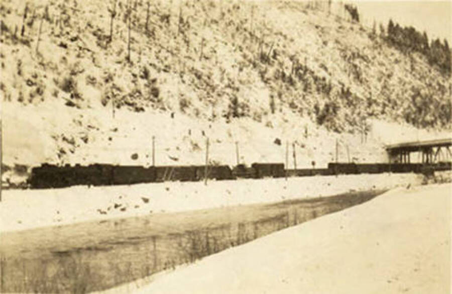 A view of the train in wintertime, across the creek, with a portion of the bridge in the background. Back of the photo reads 'Avery Valley Freight train pulling out. Feb. 1939'.