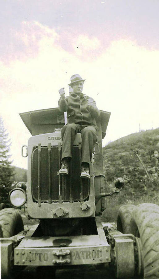 A CCC barracks leader poses atop a tractor with a cigarette in his mouth. CCC Camp Big Creek #2, F-132. Back of the photo reads: 'Bill Whitley (our barracks leader) from Kentucky. Great guy.'