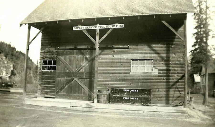A building is shown at CCC Camp Big Creek #2, F-132, with a sign that reads: 'Forest Service Tool house F-132'. There is also a chest on the porch that reads: 'Fire Only'. Back of the photo reads: 'Supply building at camp'.