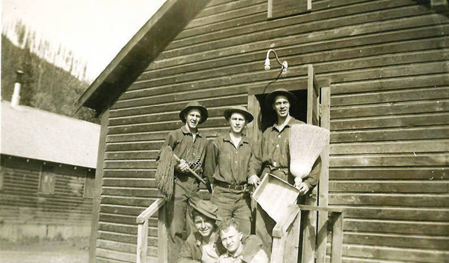 A group of CCC men pose in front of a barrack with various cleaning tools. CCC Camp Big Creek #2, F-132. Back of the photo reads: 'Sat. morning clean up - getting ready for barracks inspection'.