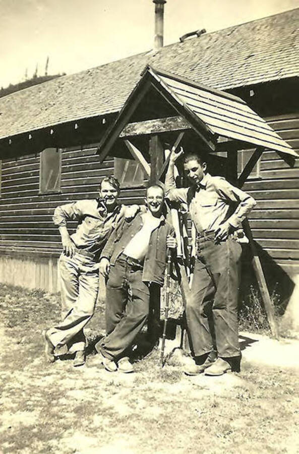 A group of CCC men pose along the side of a barrack. The man in the middle is leaning on some sort of cane. CCC Camp Big Creek #2, F-132. Back of the photo reads: 'Normen Leubbert (in middle) and friends CCC Camp 531 Pritchard, Idaho.'