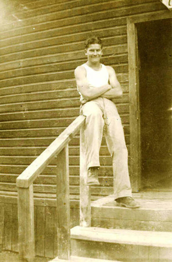 A CCC man poses in front of the barracks. CCC Camp Big Creek #2, F-132. Back of the photo reads: 'John (Dad) Barracks 7 CCC Pritchard, Idaho 1939'.