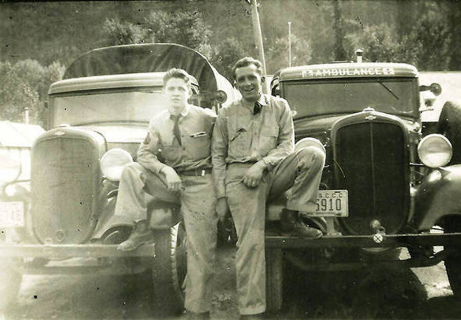 Two CCC Drivers posed in front of their vehicles. The truck on the right is labeled 'ambulance'. CCC Camp Big Creek #2, F-132. Back of photo reads: 'Our Rec truck and ambulance 'Red?' on left and Smoky Gosselt on right - drivers.'