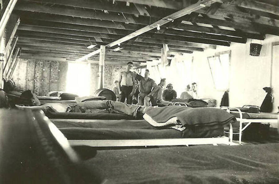 Several CCC men lounging in the barracks, several cots in the foreground. CCC Camp Big Creek #2, F-132.