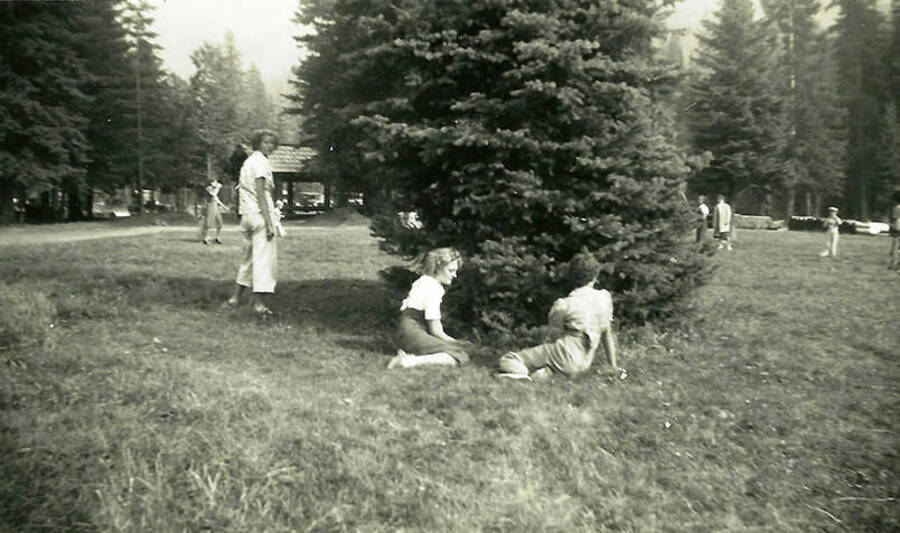 Three women in the foreground of a photo depicting Shoshone County Park. Back of the photo reads: 'Shoshone Co. Park Shelter house in background. We built several throughout the park.